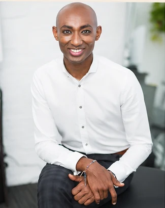 Daniel Agegnehu, founder of EthioRoot Naturals, seated and smiling in a white shirt.